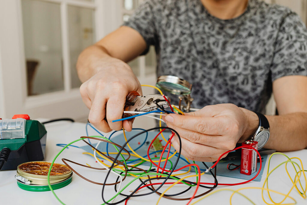 Person working with colorful wires on a table while practicing skills for electrician certification.