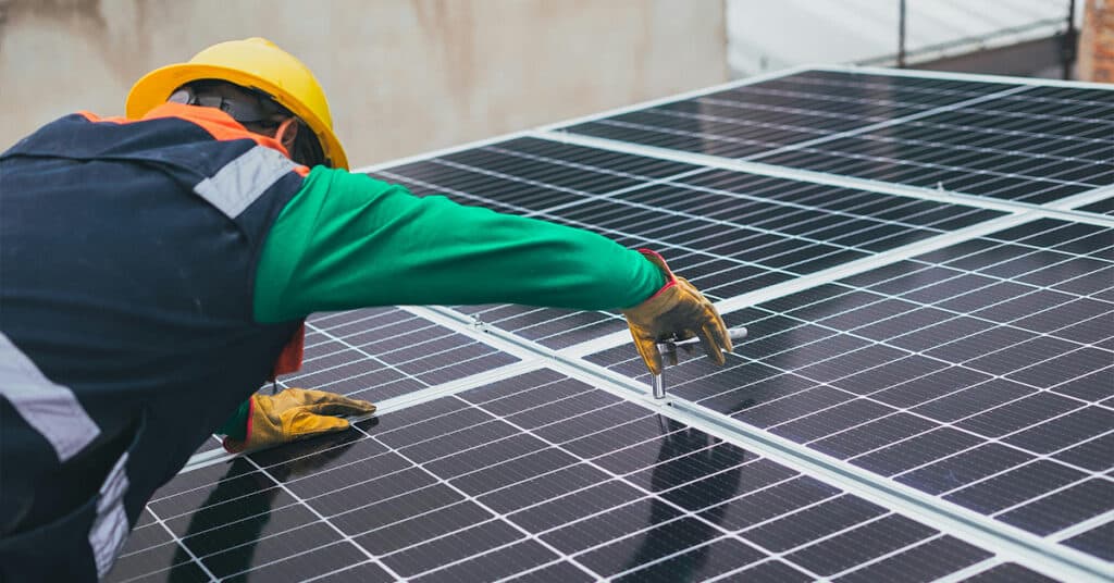 Worker installing solar panels on a roof, illustrating tasks that influence electrician salary.