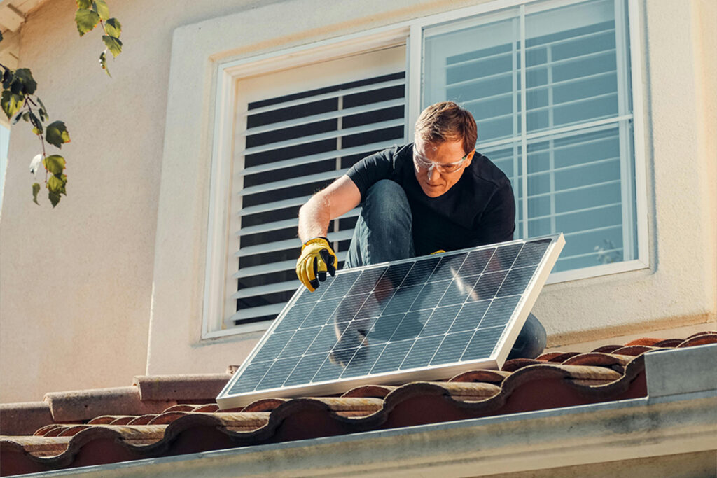 Worker placing a solar panel on a rooftop, reflecting work tied to electrician salary.