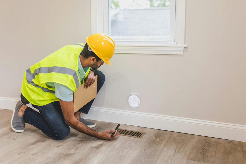 A technician inspects a floor vent during a service visit, showing tasks included in his monthly HVAC salary.