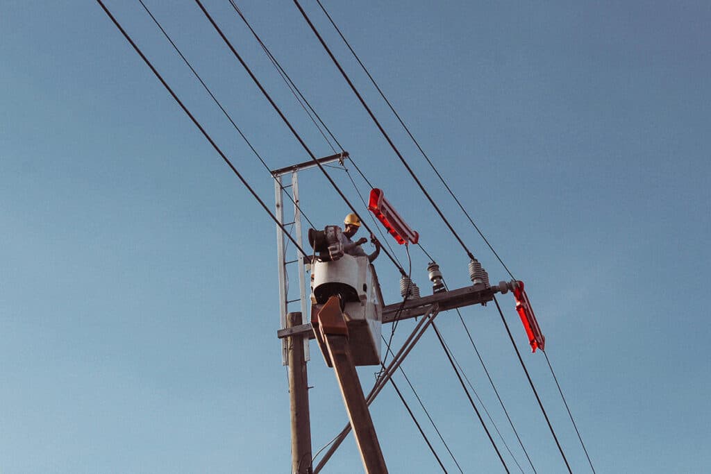 Worker in a bucket truck inspecting overhead power lines, a part of electrician description duties.